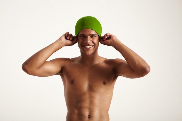 happy smiling African American swimmer putting on his green swimming cap looking on white