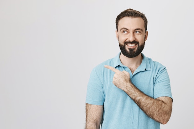 Happy smiling caucasian guy with beard pointing left