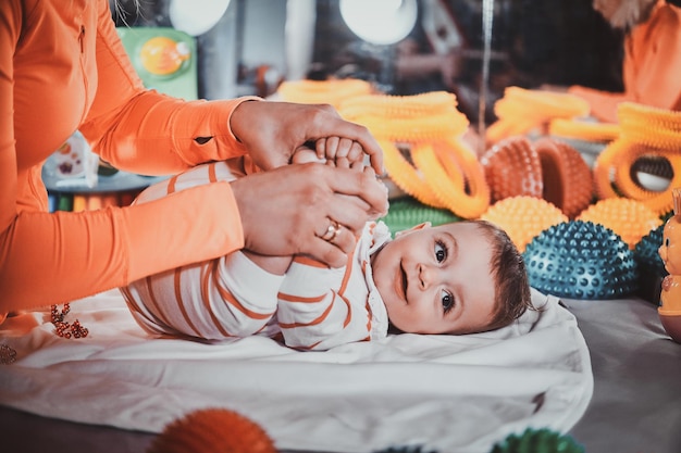 Free photo happy smiling cute toddler is lying on the special table surrounded by ortopedic toys while expirienced masseur making massage for him.