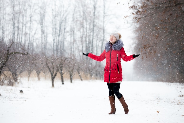 Happy smiling female in red winter jacket enjoys the snow, outdoors, in park