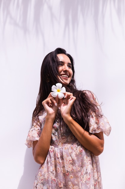 Happy smiling long haired woman in dress stands on white wall