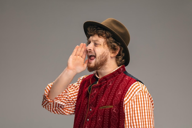 Happy smiling man dressed in traditional austrian or bavarian costume gesturing isolated on grey