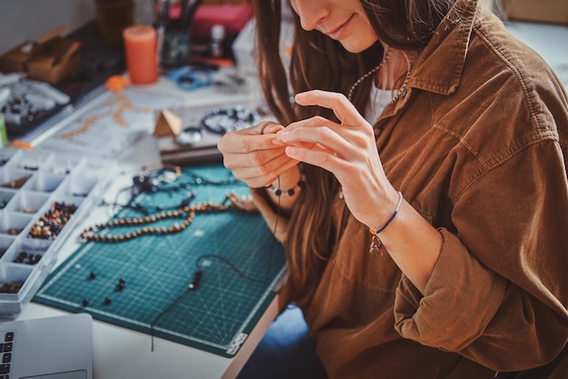 Free photo happy smiling woman is working on beads jewellery at her own workplace.