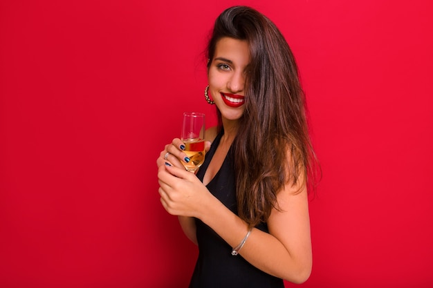 Happy smiling woman on red background celebrating new year, wearing luxury dress and holding champagne.