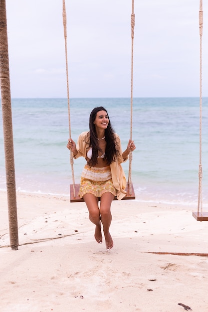 Free Photo happy smiling woman on swing at beach,day warm light.