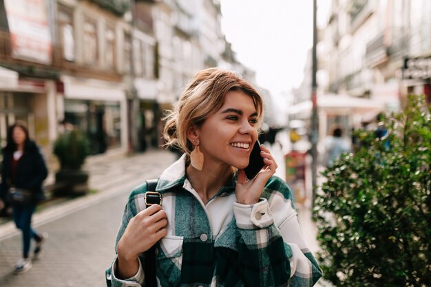 Happy smiling woman with collected blond hair talking on smartphone on the street