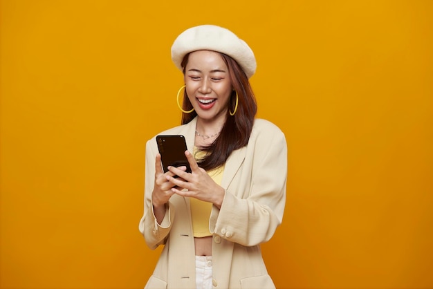 Happy smiling young asian woman using mobile phone isolated on y