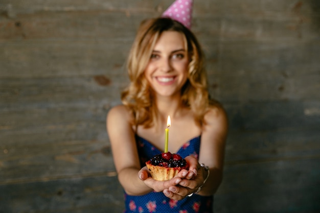 Happy smiling young woman celebrating her birthday party, holds a fruit cupcake with candle