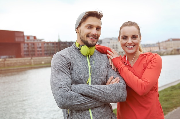 Free photo happy sporty couple posing against the river