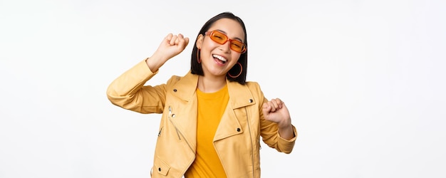 Happy stylish korean girl in sunglasses dancing and laughing smiling carefree standing over white background Copy space