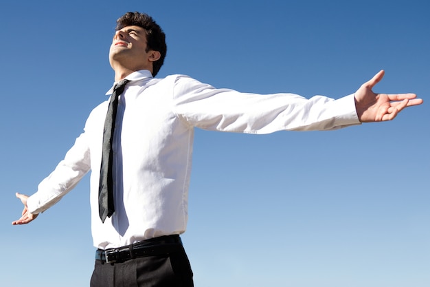 Happy successful business man raised arms with sky in the background