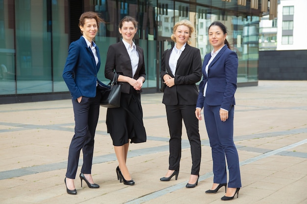 Free Photo happy successful female business group standing together near office building, posing, looking at camera and smiling. full length, front view. businesswomen group portrait concept