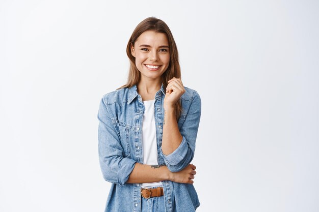 Happy successful woman standing in casual outfit, smiling pleased and looking confident, standing on white