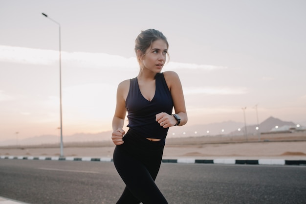 Happy sunny morning moments of hardworking motivated amazing young woman in sportswear running on road in early morning un tropical country. Training, workout, healthy lifestyle