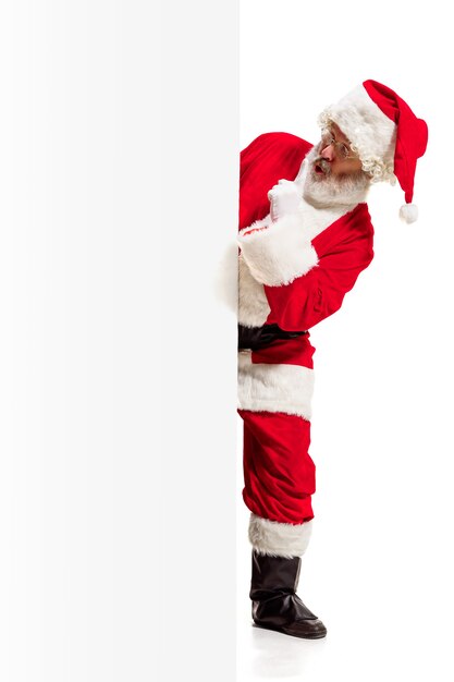 Happy surprised Santa Claus pointing on blank advertisement banner background with copy space. Smiling senior man showing at white blank of empty poster