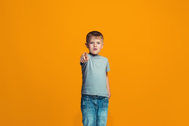 The happy teen boy pointing to you, half length closeup portrait on orange space.