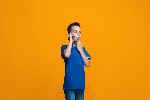 The happy teen boy standing and smiling against orange background.