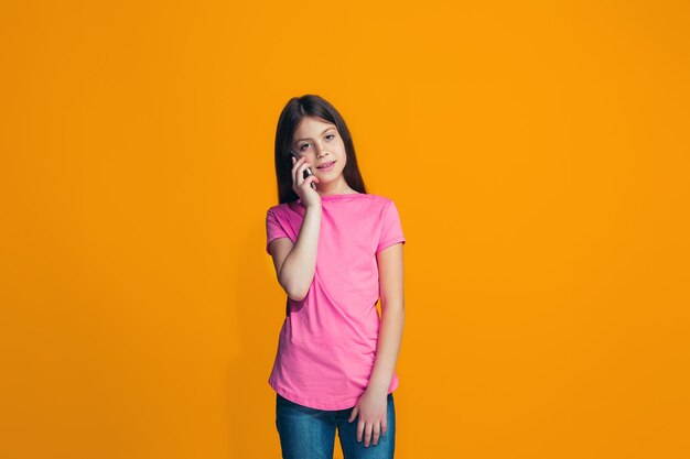 The happy teen girl standing and smiling against orange.