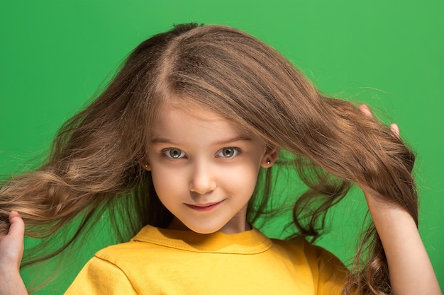 Happy teen girl standing, smiling isolated on trendy green studio background. Beautiful female portrait. Young satisfy girl. Human emotions, facial expression concept. Front view.