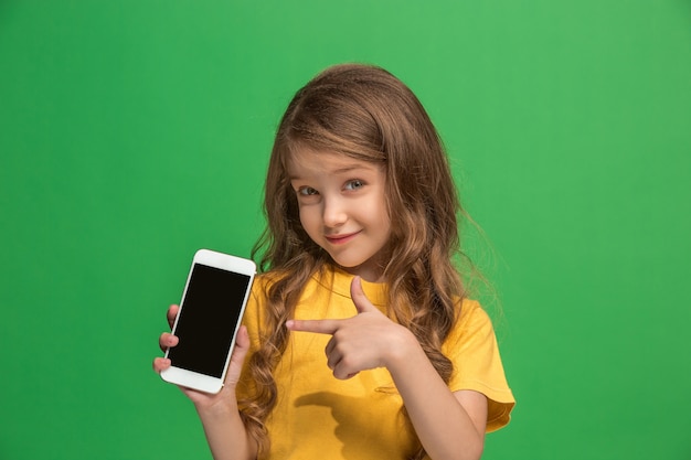 Happy teen girl standing, smiling with mobile phone over trendy green. Beautiful female half-length portrait