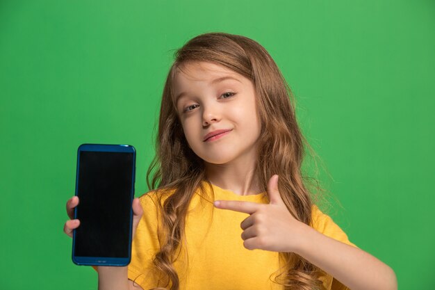 Happy teen girl standing, smiling with mobile phone over trendy green studio background.