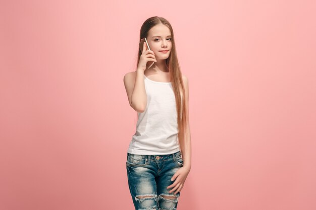 Happy teen girl standing, smiling with mobile phone over trendy pink studio.