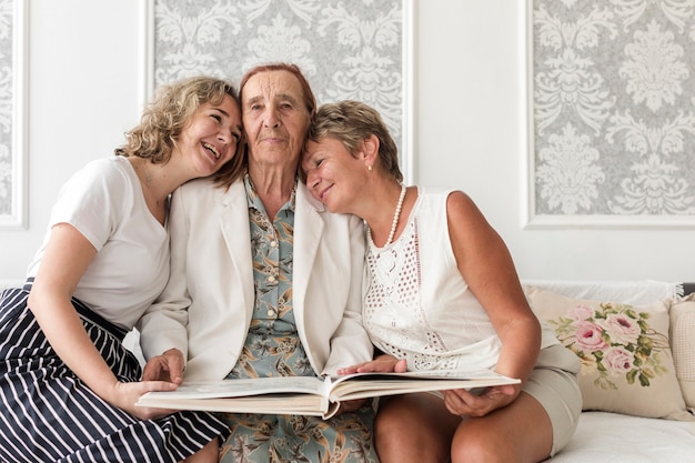 Free photo happy three generation women sitting on sofa with holding photo album