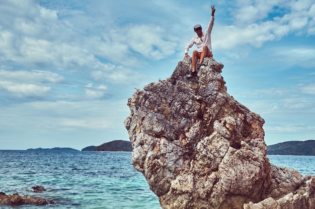 A happy tourist sits on a big rocky stalactite reef on the shore of the ocean. Philippine Islands. Pacific ocean.