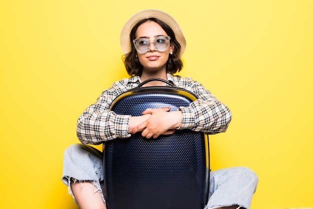 Free photo happy tourist woman in summer casual clothes, hat sit with suitcase, looking aside isolated on yellow orange wall. girl traveling abroad to travel on weekends getaway. air flight concept