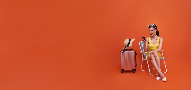 Free photo happy traveler tourist woman sitting on chair with suitcase using mobile cell phone