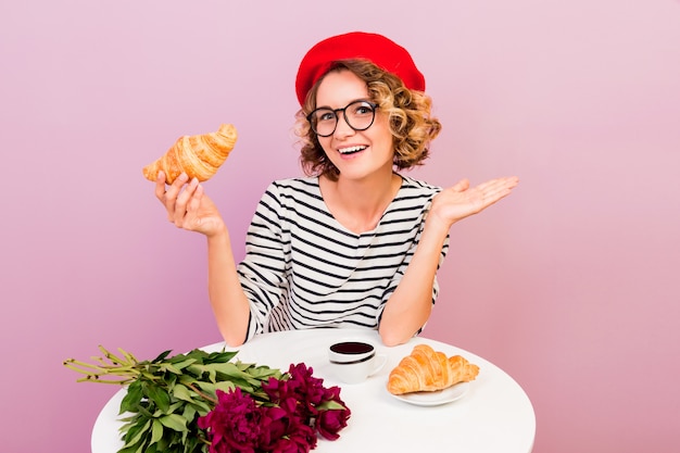 Free Photo happy traveling woman in france eating croissans with coffee, sits by the table on pink.