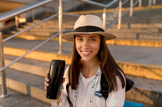 Free photo happy traveling woman with backpack and hat holding thermos