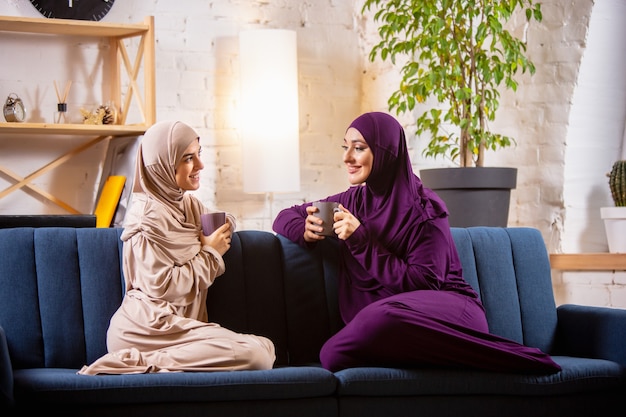 Happy two muslim women at home during lesson, studying near computer, online education