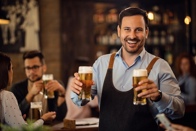 Happy waiter holding two glasses of beer and looking at camera while working in a pub