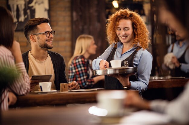 Happy waitress giving coffee to customers while serving them in coffee shop