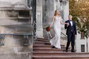 Free photo happy wedding couple is coming out of the church on the stairs are holding hands together