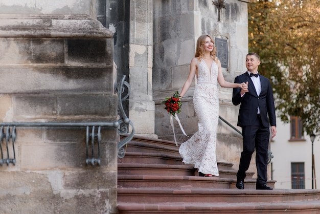 Happy wedding couple is coming out of the church on the stairs are holding hands together