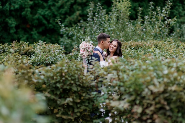 Free photo happy wedding couple is smiling and kissing in the high green bushes