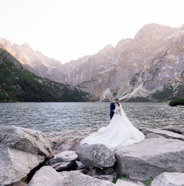 Free Photo happy wedding couple is standing in front of lake surrounded with mountains on the huge rock