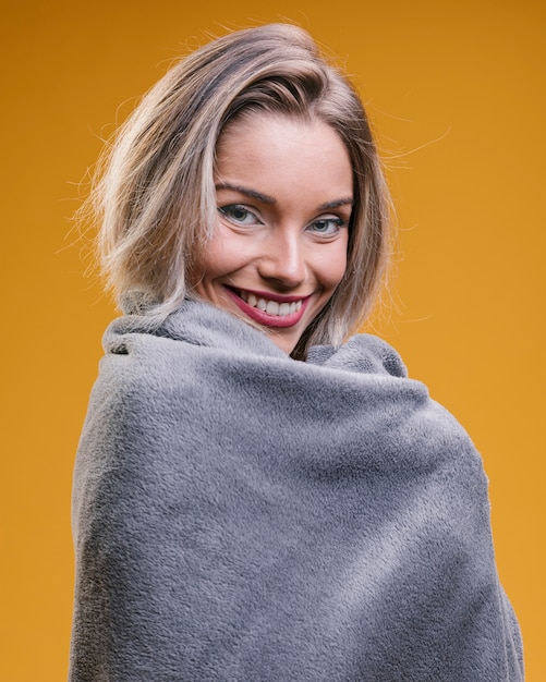 Free photo happy woman covered with warm blanket against yellow background