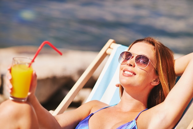 Happy woman drinking a orange juice on the beach