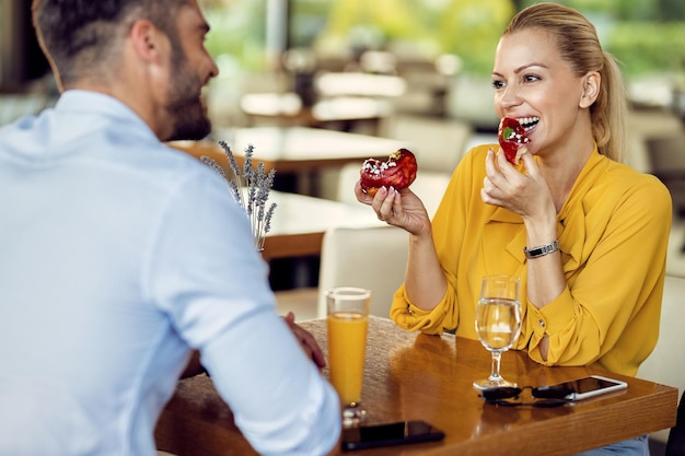 Free photo happy woman eating donuts and talking to her boyfriend in a cafe