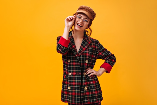 Free Photo happy woman in eyeglasses, cap and plaid jacket smiling on orange wall