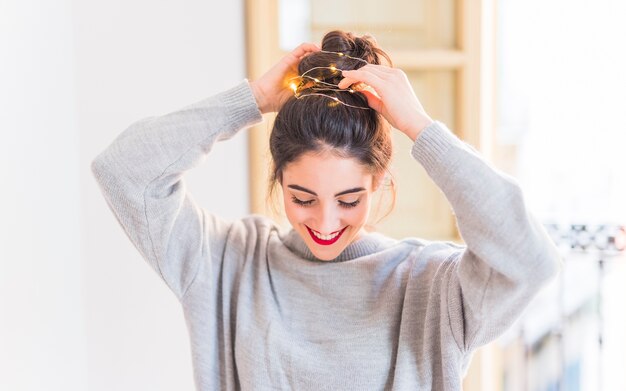 Happy woman in grey holding hands on hair with garland