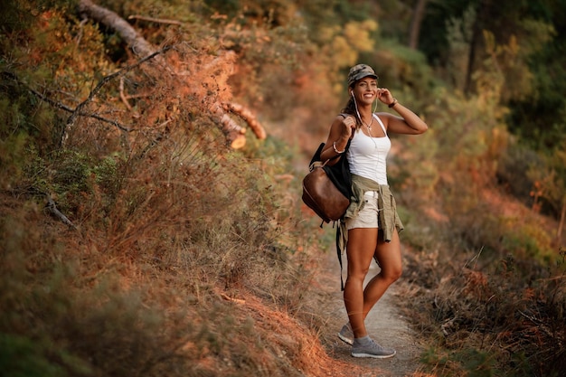 Free Photo happy woman hiking while listening music on earphones in the forest