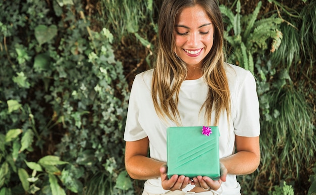 Free Photo happy woman holding green gift box in front of green leaves background