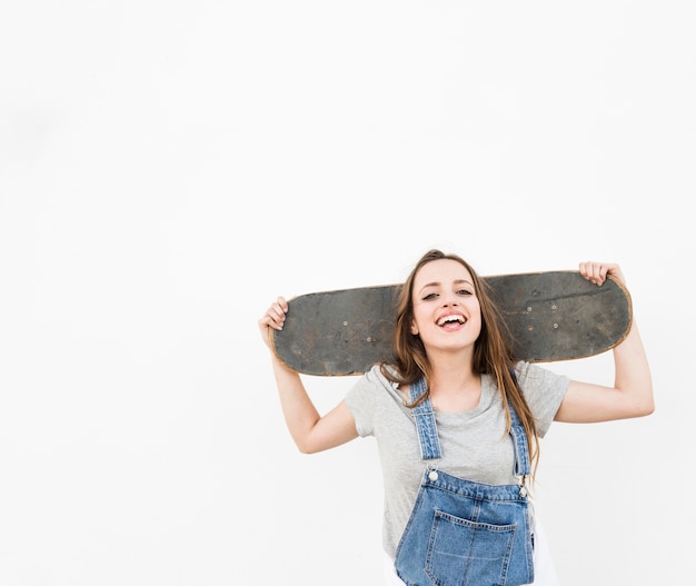 Happy woman holding skateboard on her shoulder against white backdrop