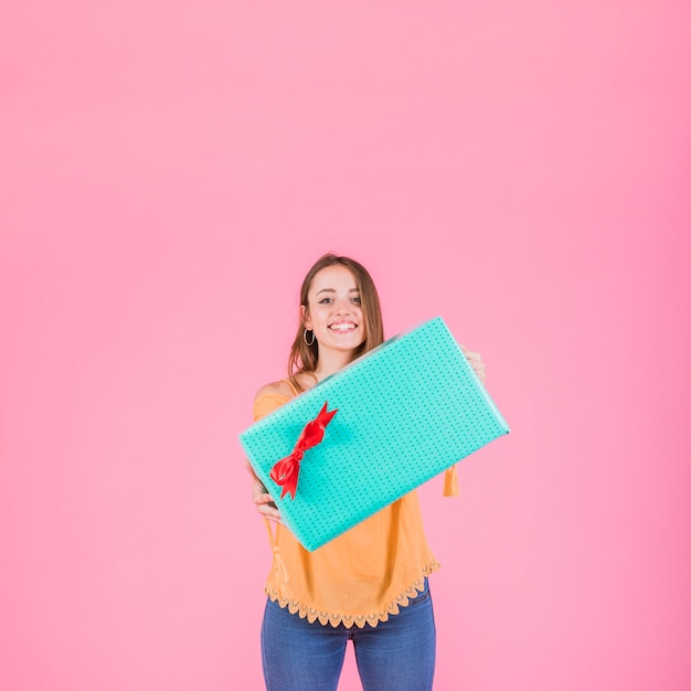 Free Photo happy woman holding wrapped gift box against pink background