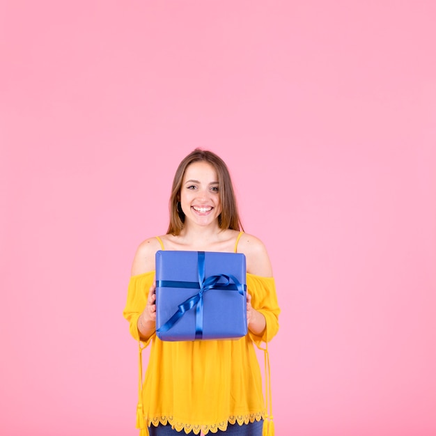 Free Photo happy woman holding wrapped present standing against pink background