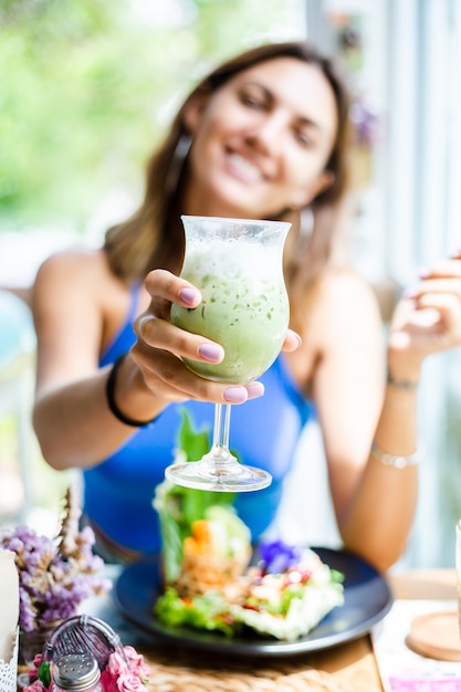 Happy woman holds japanese matcha green tea with ice in glass in cafe Female with healthy antioxidant beverage in summer cute cafe